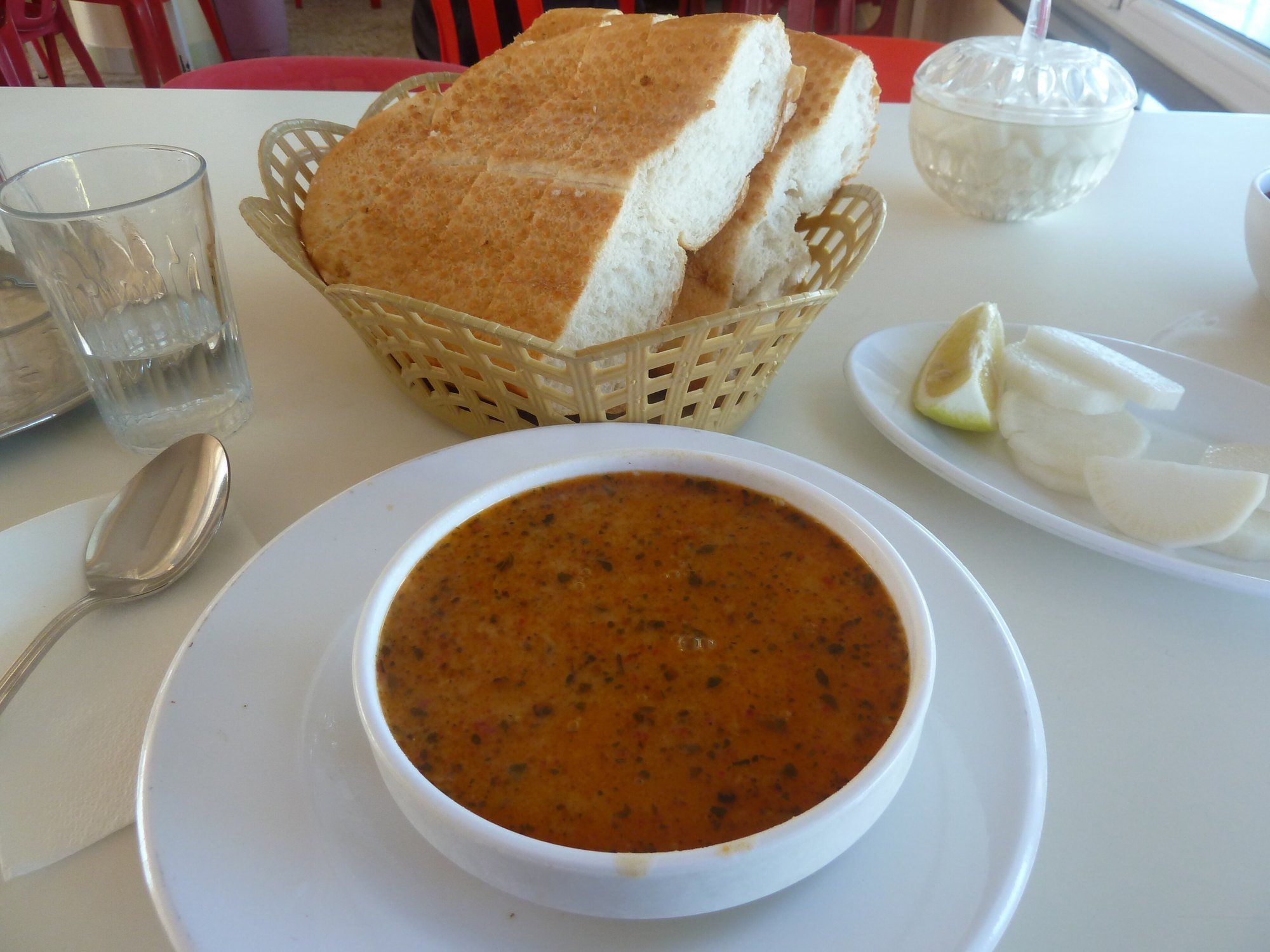 Beyaz kâsede naneli ezogelin çorbası, arkada ekmek sepeti ve limon