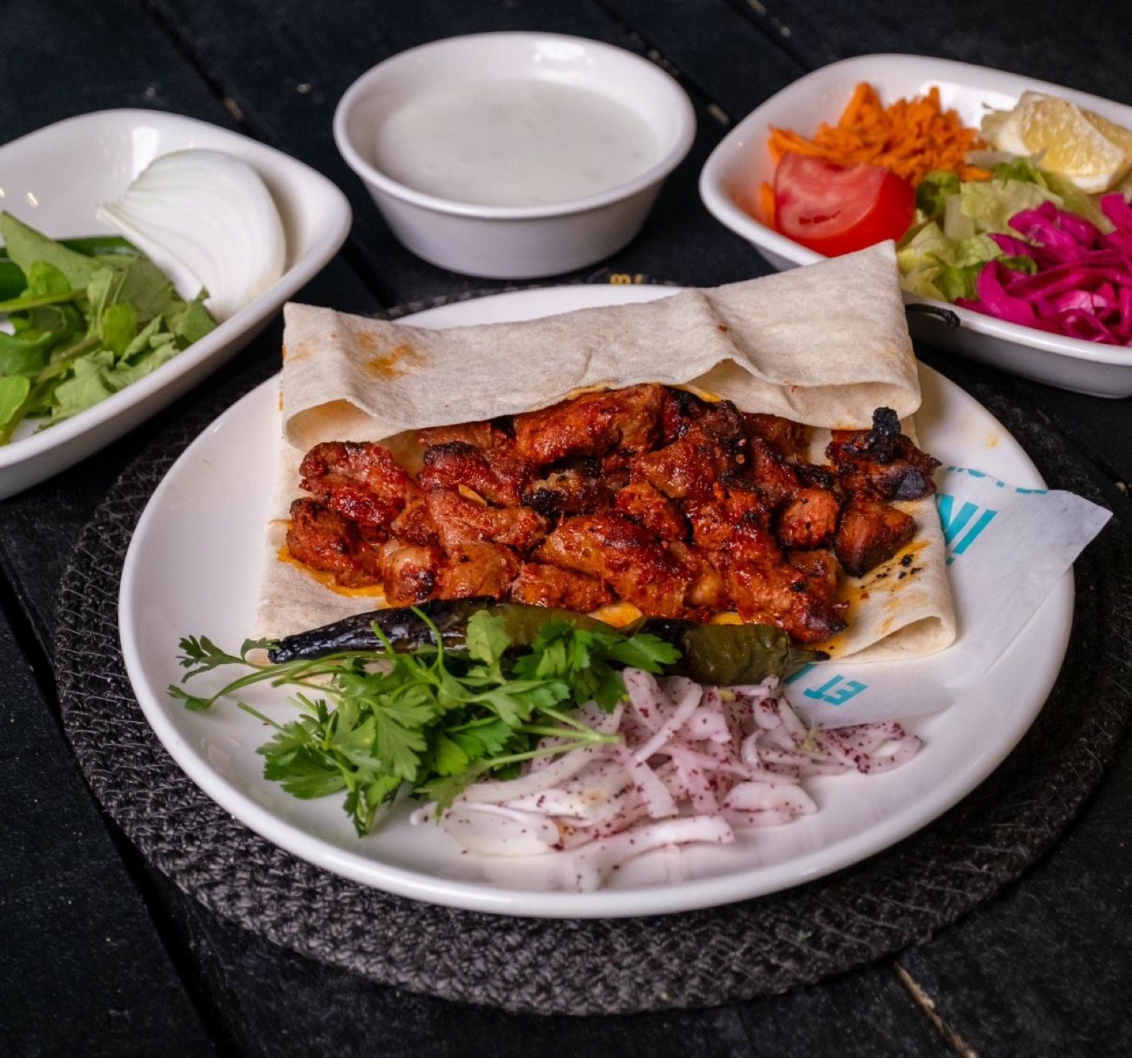 Lavaş üzerinde kuşbaşı porsiyon, sumaklı soğan, közlenmiş biber, yanında yoğurt ve salata