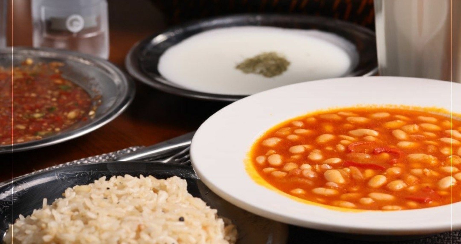 Beyaz kâsede etli kuru fasulye, yanında pirinç pilavı ve yoğurt çorbası