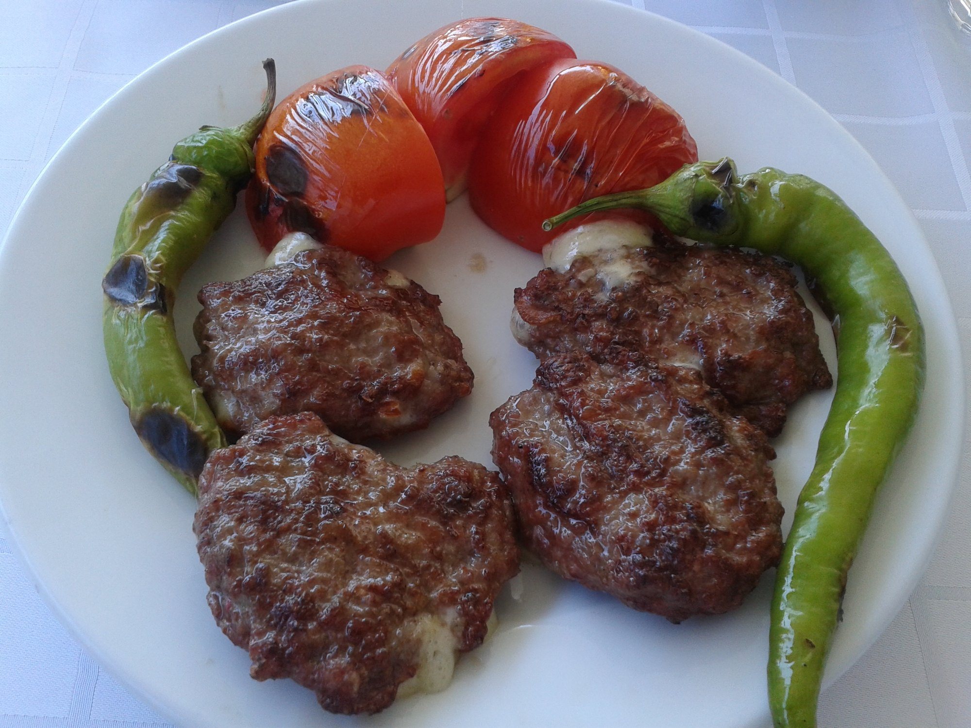 Kaşar dolgulu ızgara köfteler, közlenmiş domates ve sivri biberle beyaz tabakta