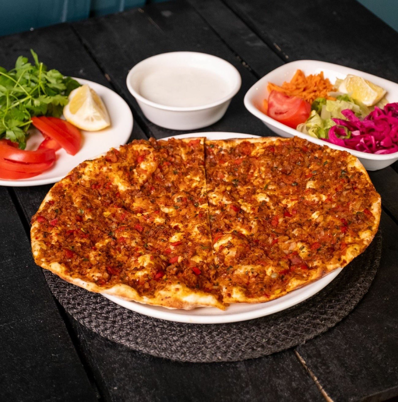 Beyaz tabakta Urfa lahmacun, yanında maydanoz, limon, yoğurt ve salata