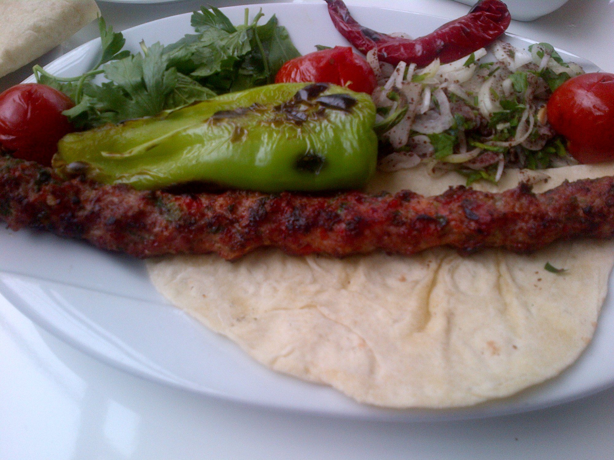 Lavaş üzerinde haşhaş kebabı, közlenmiş biber, domates, maydanoz ve soğan salatası