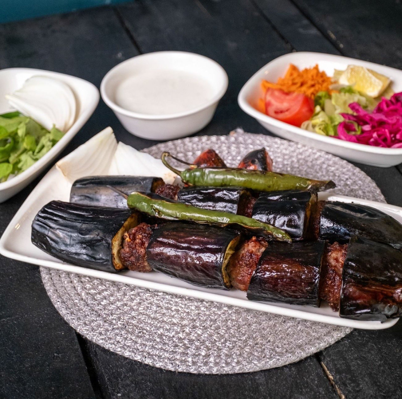Uzun tabakta patlıcanlı kebap ve közlenmiş biber, yanında yoğurt ve salata