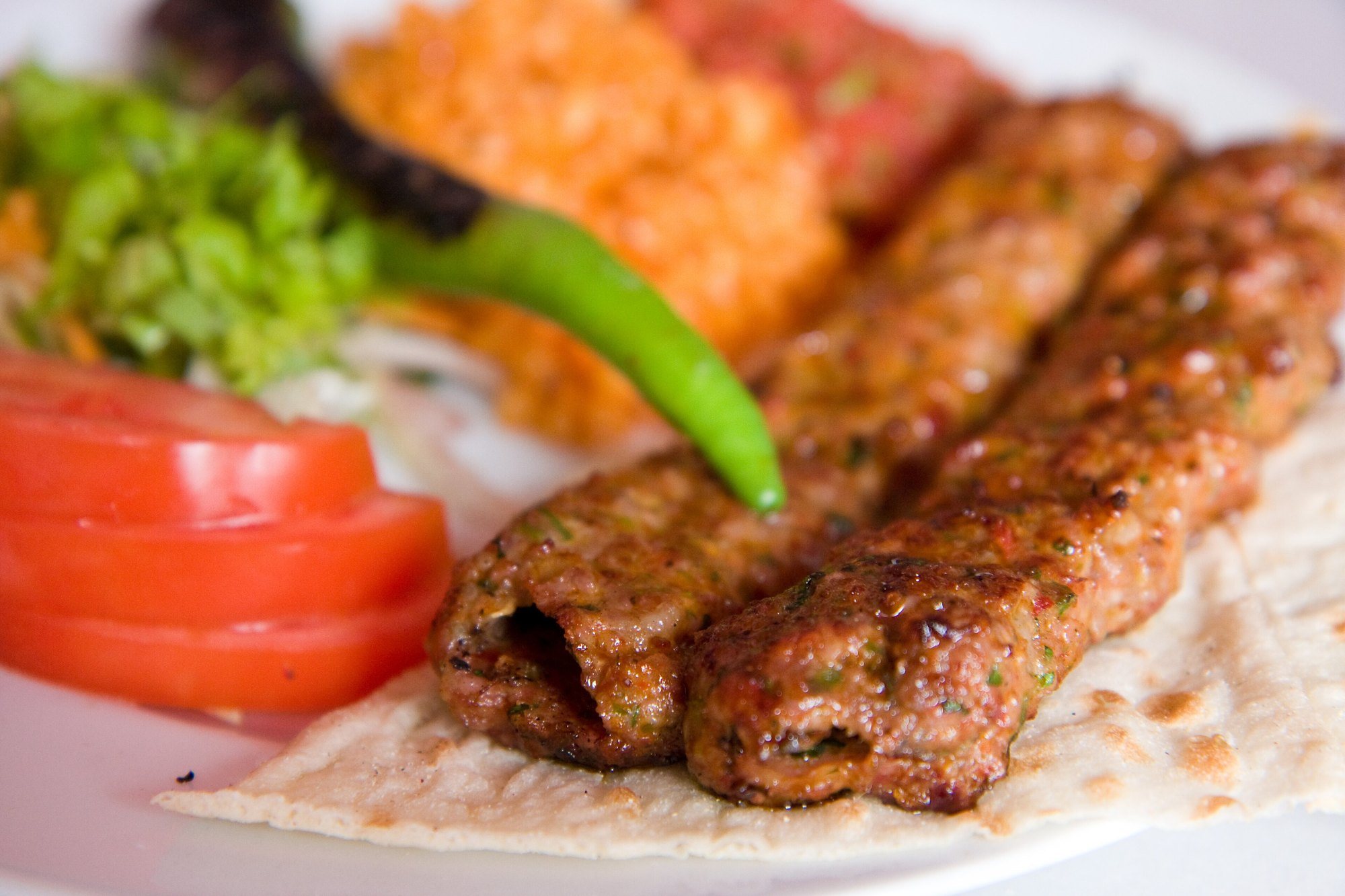 Lavaş üzerinde iki şiş közlenmiş Adana kebabı, yanında domates ve biber