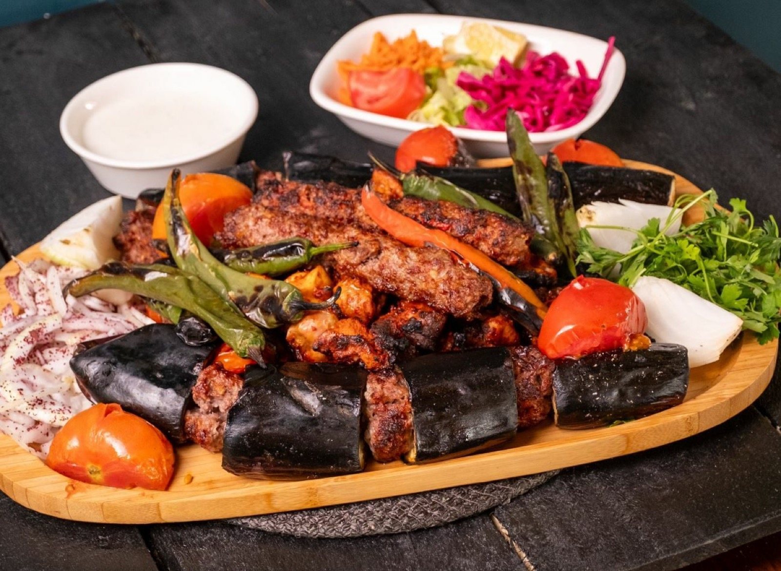 Ahşap tahtada karışık kebap: patlıcanlı, adana, tavuk şiş, közlenmiş sebzeler, yanında salata ve yoğurt