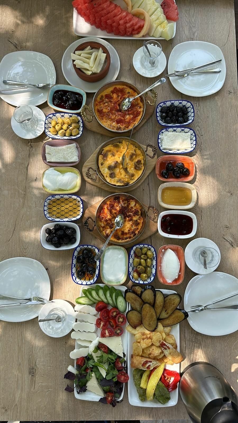 Ahşap masada iki kişilik serpme kahvaltı: peynirler, zeytin, sahanda menemen ve reçeller
